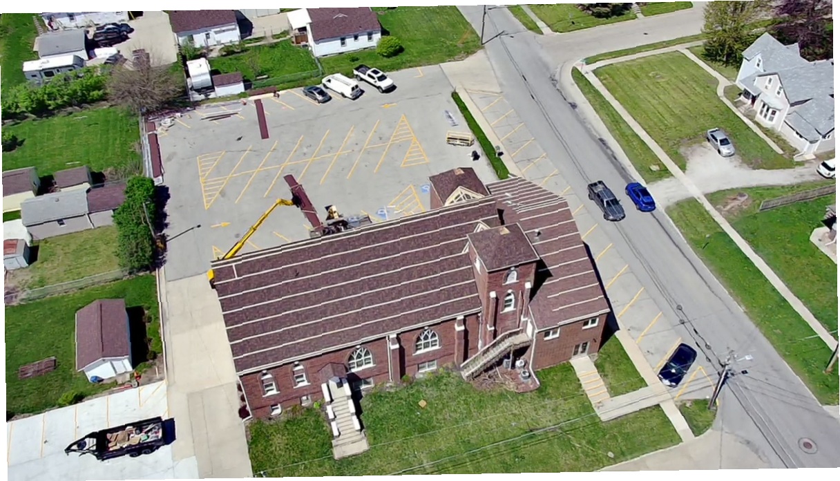 Aerial view of a large brick building roofing project with boom lift on site
