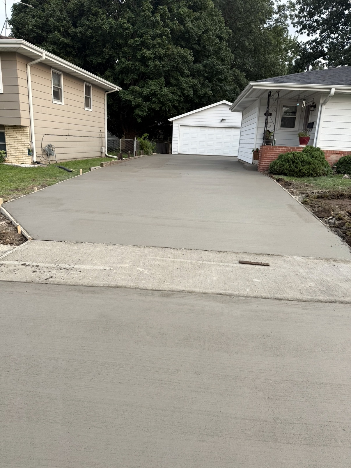 Freshly poured concrete driveway between two homes leading to a garage